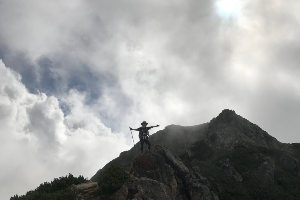 稜線で両手を広げる登山者と岩峰