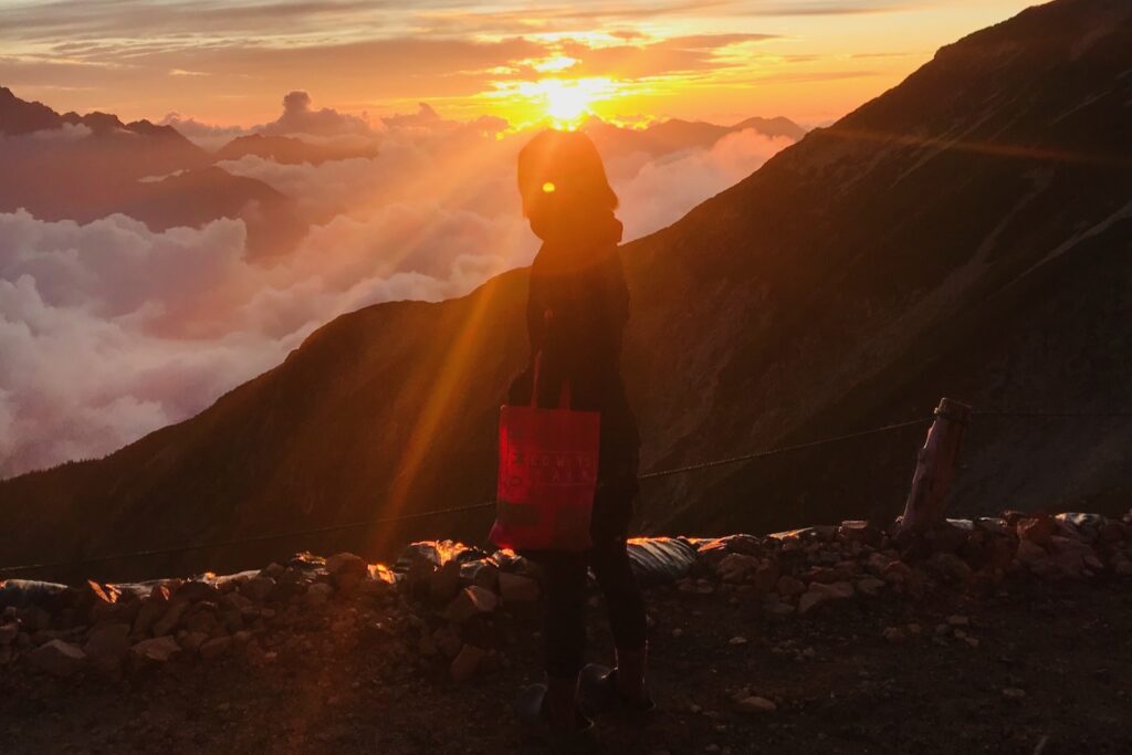 夕陽を背に雲海の前に立つ登山者のシルエット