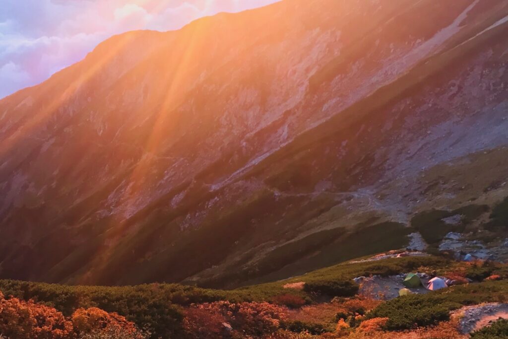 雲間から差す夕陽の光線と唐松岳頂上山荘のテント場