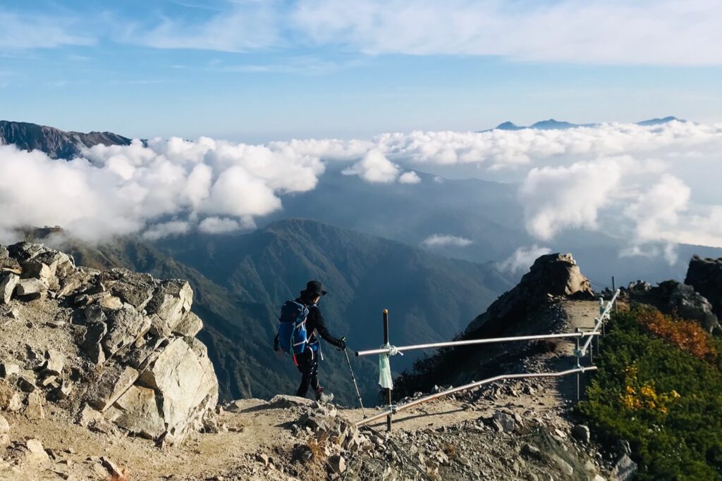 雲海を眼下に岩場の稜線を下る登山者