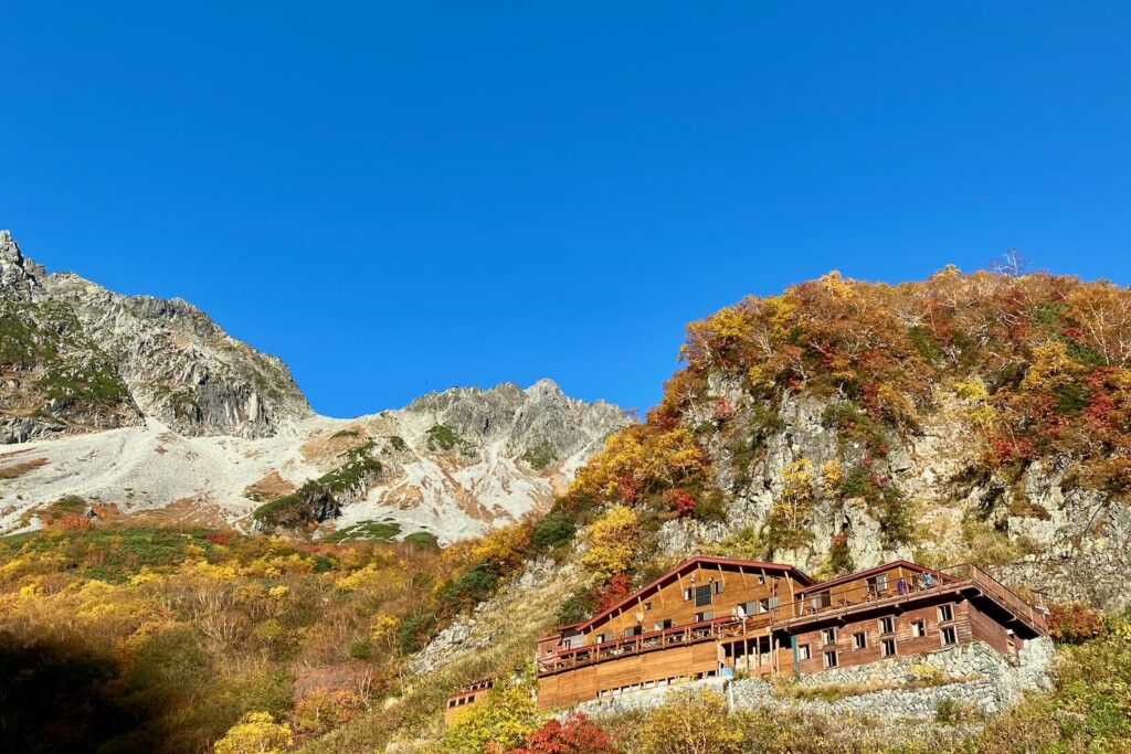 紅葉の中に建つ涸沢小屋とそびえる岩壁