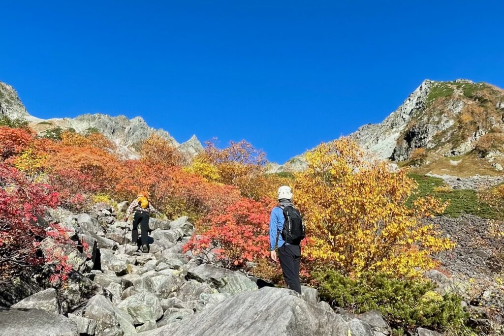 紅葉に囲まれた岩場の登山道を登る登山者