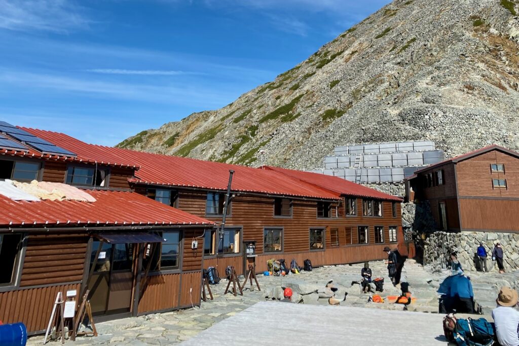 赤い屋根の穂高岳山荘と休憩する登山者たち