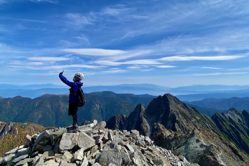奥穂高岳山頂の岩の上に立つ登山者