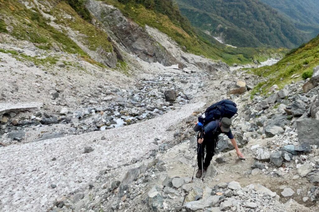 雪渓脇の岩場を登る登山者