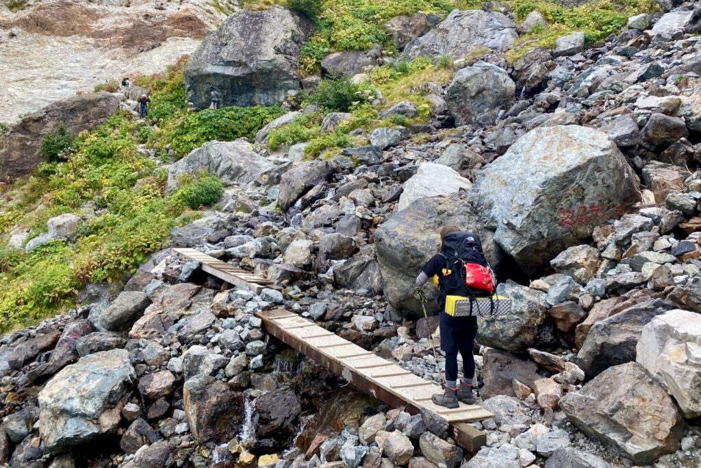 岩場に架かる木の桟橋を渡る登山者