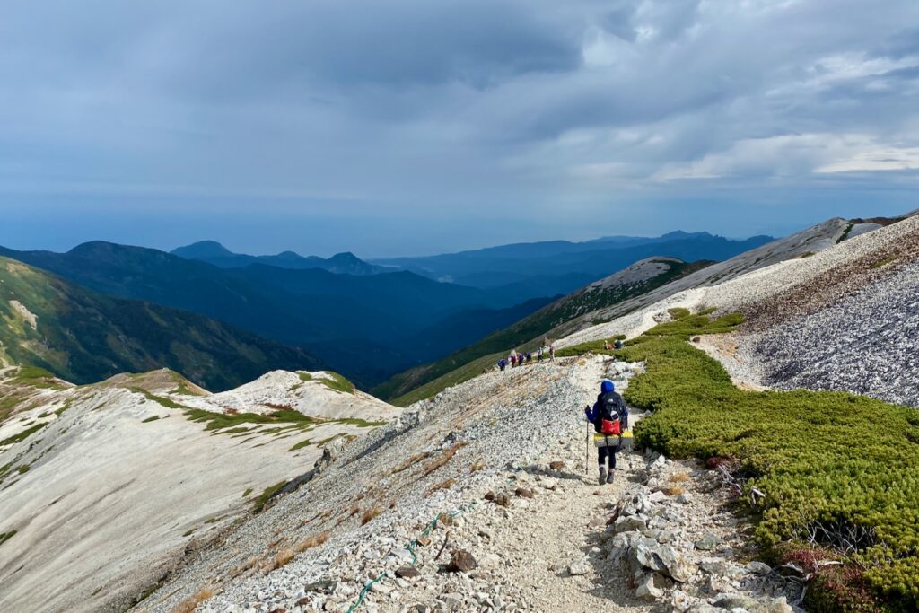白い砂礫の稜線を下る登山者の列
