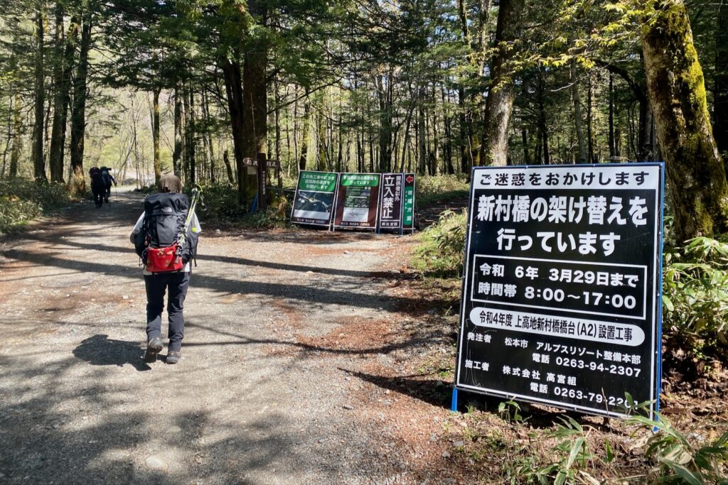 新村橋架け替え工事の案内看板の横を歩く登山者