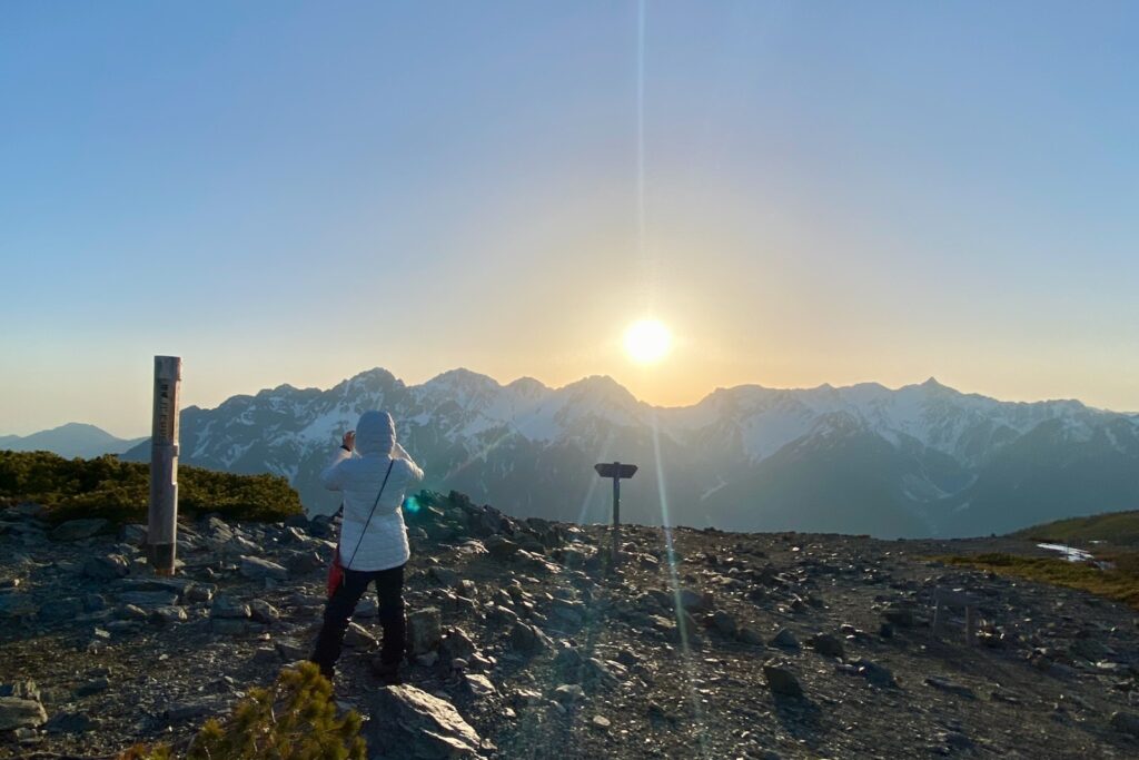 蝶ヶ岳山頂で夕日を撮影する登山者と残雪の穂高連峰