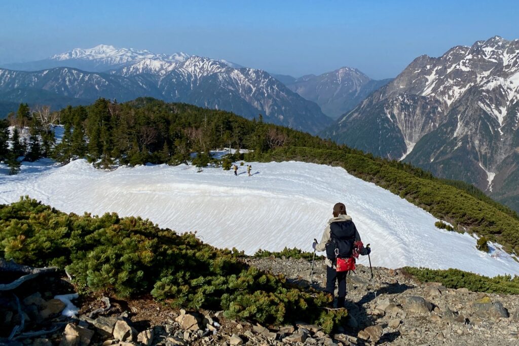 長塀尾根の雪田を下る登山者と遠くに広がる残雪の山々