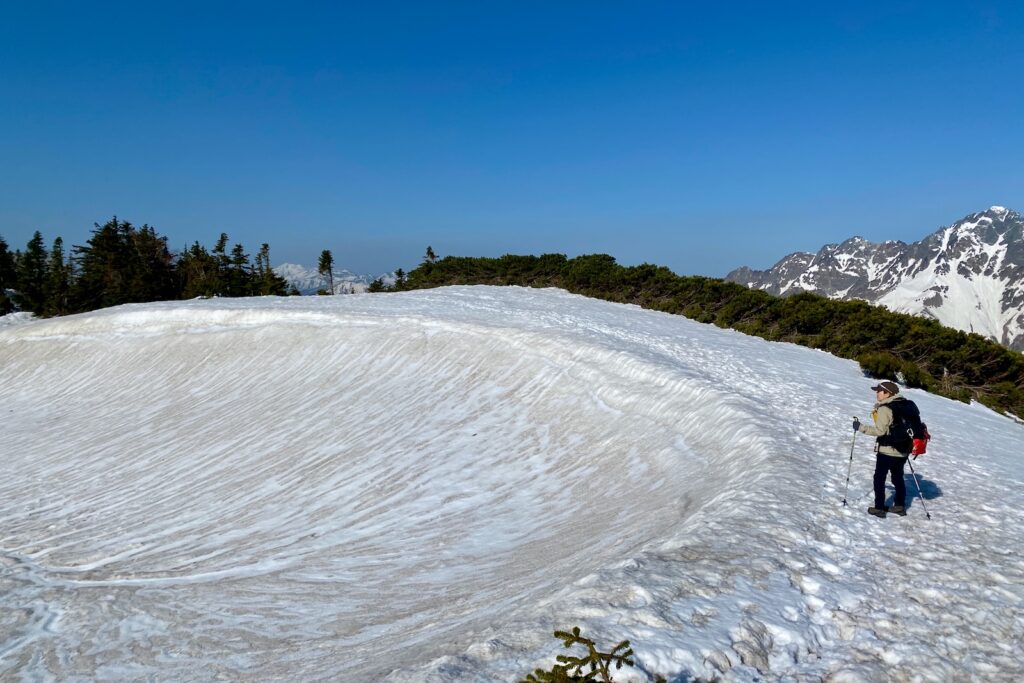 蝶ヶ岳の稜線に残る大きな雪田と眺める登山者、奥に穂高連峰