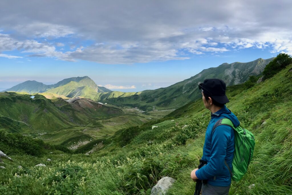 朝日に照らされた山々を眺める緑のアタックザックの登山者