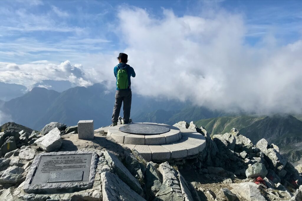 雄山山頂の方位盤に立って雲海を見渡す登山者