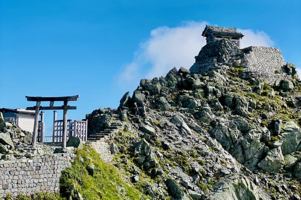 青空の下、岩の山頂に建つ雄山神社峰本社と鳥居