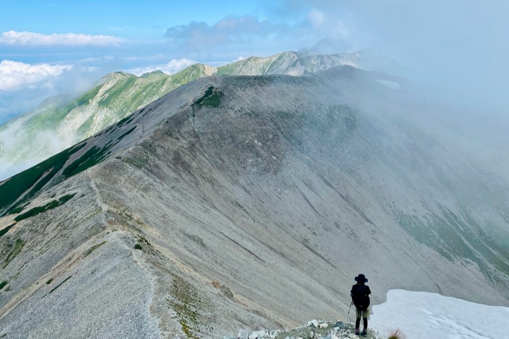 ガスがかかり始めた砂礫の稜線を歩く登山者