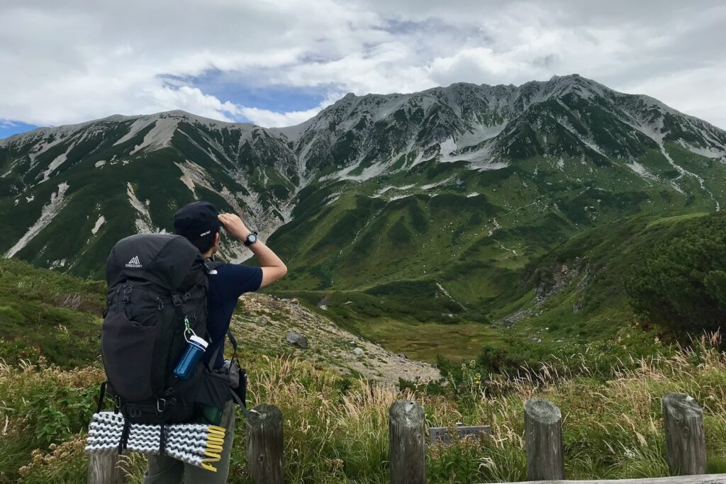 大きなザックを背負って立山連峰を見上げる登山者